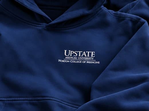 Close-up of the white Upstate Medical University, Norton College of Medicine wordmark on the left chest
